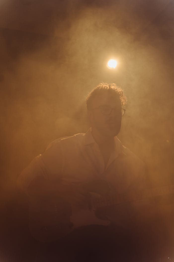 Silhouetted musician playing guitar on stage with dramatic fog and lighting.